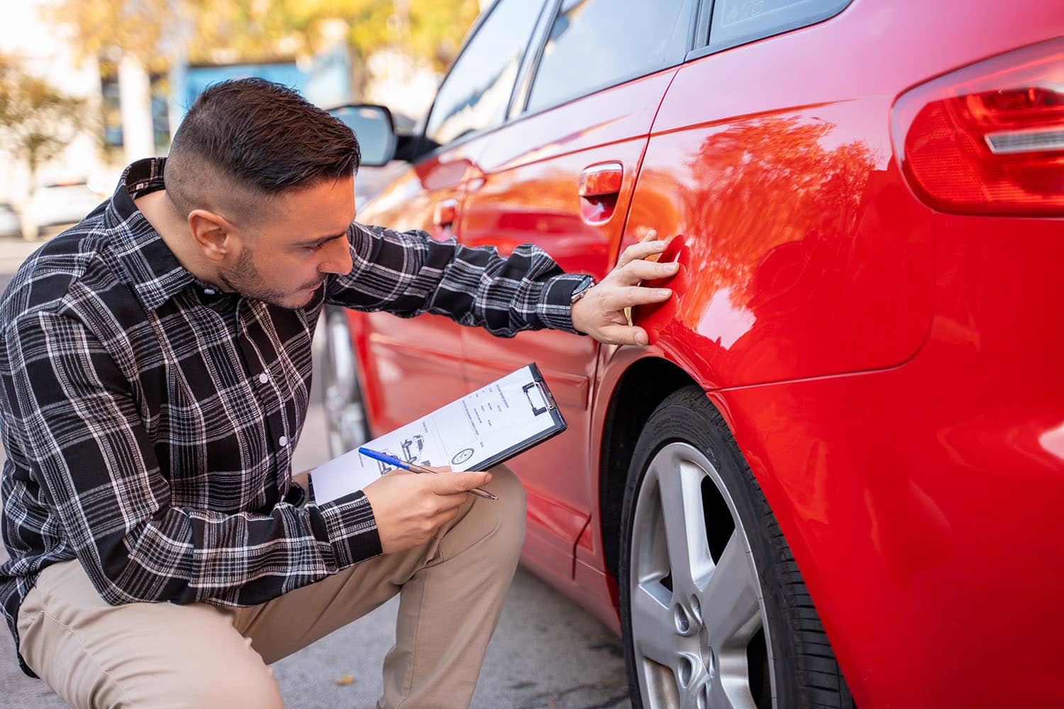 Dent Doctor technician crouched down next to car inspecting a door ding to give an estimate
