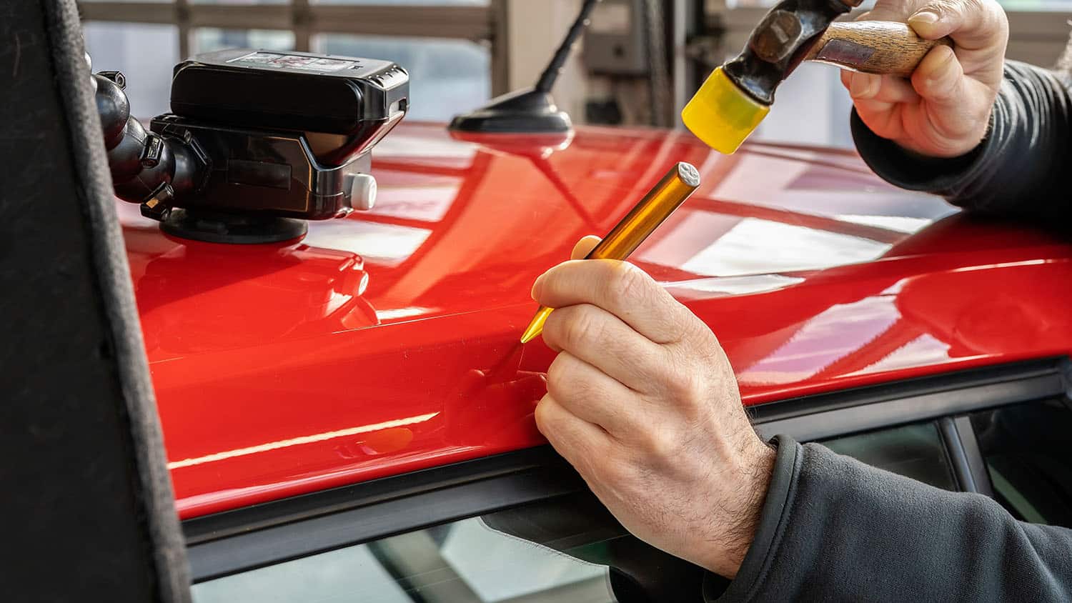Technician performing car hail damage repair on a red vehicle roof using paintless dent repair tools in Montrose, CO